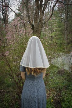 a woman wearing a veil and dress in front of a tree with pink flowers on it