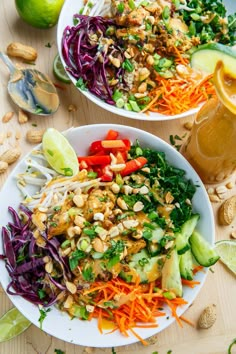 two white bowls filled with salad on top of a wooden table next to limes