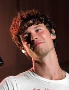 a young man with curly hair is singing into a microphone and looking up at the sky