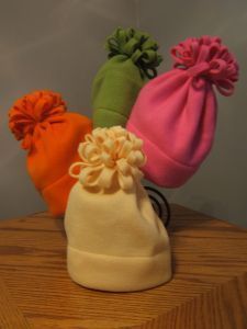 three beanies are sitting on top of a wooden table and one is pink, green, orange, and white