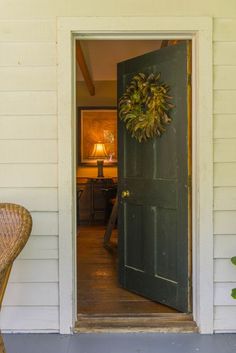 an open door with a wreath hanging on the side of it next to a wicker chair