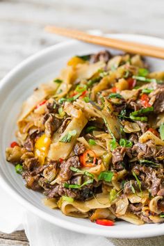 a white plate topped with noodles and meat next to chopsticks on a table