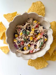 a bowl filled with chicken salad surrounded by tortilla chips on a white surface