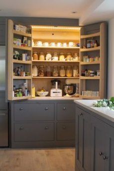 a kitchen with gray cabinets and shelves filled with food on top of wooden flooring