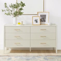 a white dresser with two framed pictures on it and a plant in front of it