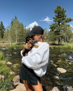 a woman is holding a small dog in her arms while standing on rocks near a river