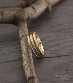 two gold wedding rings sitting on top of a piece of driftwood, with the ring resting on it's side