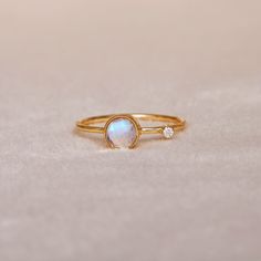 a gold ring with an opal and two diamonds on the side, sitting on a white surface