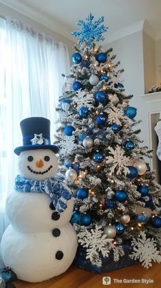 a decorated christmas tree and snowman in front of a window with blue ornaments on it