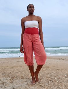 a woman standing on top of a sandy beach next to the ocean with her hands in her pockets