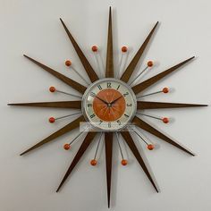 an orange and white clock mounted to the side of a wall next to wooden sticks