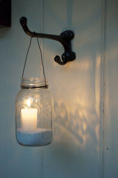 a candle is lit in a mason jar hanging from a hook on a white wall