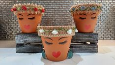 three clay pots with faces painted on them and flowers in their hair are sitting on a table