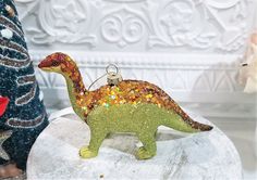 a glass ornament shaped like a dinosaur on top of a white table next to a christmas tree