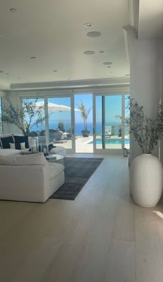 a living room with white furniture and large glass doors leading to an ocean side swimming pool