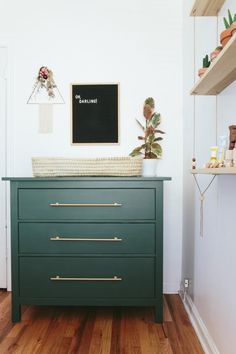 a green dresser with gold handles in a white room next to a black and white wall