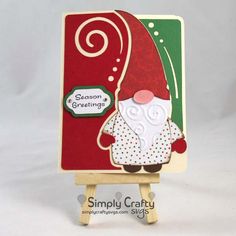 a card with an image of a santa clause standing on a easel holding a sign that says seasons greetings