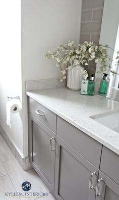 a white bathroom with gray cabinets and marble counter tops is pictured in this image, there are two vases on the vanity