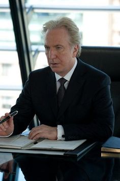 a man in a suit sitting at a desk with a book and pen on his lap