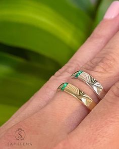 two gold rings with green stones on each one and the other hand holding another ring