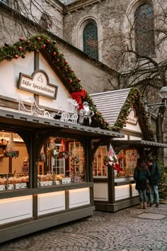 two people are standing in front of a store with christmas decorations on the roof and windows