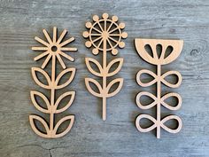 four wooden cutouts of flowers and leaves on a wood background, each with an individual's own design