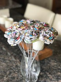 a vase filled with lots of paper flowers on top of a marble countertop next to white chairs