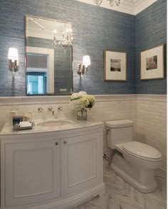 a white toilet sitting next to a sink in a bathroom under a large framed mirror