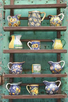 a shelf with many different vases and pitchers on it's shelves in front of a green wall