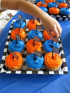 cupcakes with blue and orange frosting are being held by a child's hand