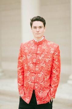 a young man wearing an orange jacket and black pants standing in front of some columns