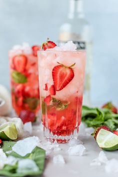 two glasses filled with ice and strawberries on top of a table next to sliced limes