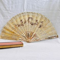 an antique hand fan next to a book on a white tablecloth covered background,