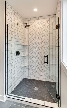 a walk in shower sitting next to a white tiled wall and floor covered in black tile