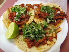 two tortillas topped with meat and vegetables on top of a white paper plate