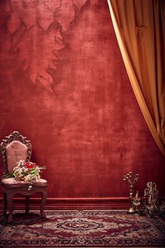 a chair sitting in front of a red wall next to a rug and vases