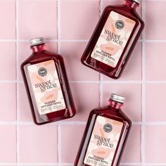 three bottles of body wash sitting on top of a pink tile wall next to each other