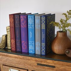 the books are lined up on the shelf next to the vase with flowers in it