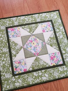 a quilted table topper on a wooden floor with flowers in the center and a black border around it