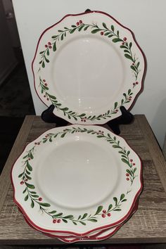 two white plates sitting on top of a wooden table covered in holly wreaths and red berries