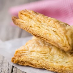 two pastries sitting on top of a piece of paper next to a pink napkin