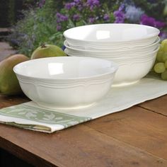 two white bowls sitting on top of a wooden table next to grapes and pears