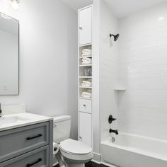 a white toilet sitting next to a bath tub in a bathroom under a mirror on top of a wooden cabinet