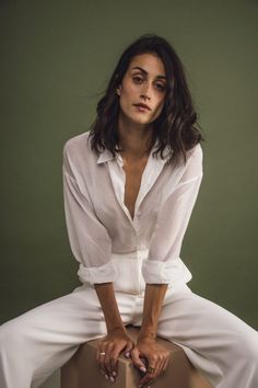 a woman sitting on top of a box wearing white pants and a white shirt, posing for the camera