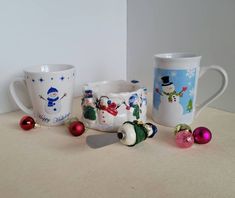 three coffee mugs decorated with snowmen and christmas decorations, sitting on a table