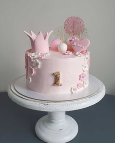 a pink birthday cake with princess decorations on top and the number one frosted in gold