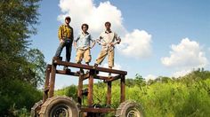 three young men standing on top of an old wooden cart in the middle of a field