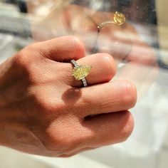 a person's hand holding a yellow diamond ring in front of a glass window