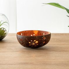 a wooden bowl sitting on top of a table next to a glass vase filled with plants