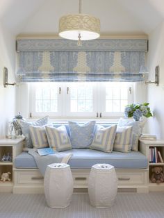 a blue and white couch sitting under a window in a living room next to two vases